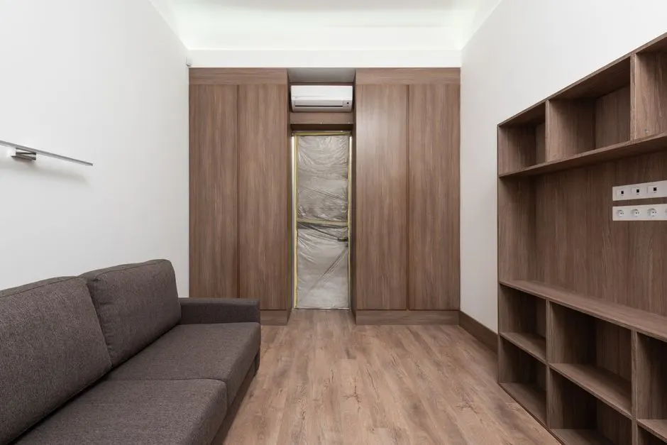 Sleek living room design featuring wooden cabinets and a gray sofa on wooden flooring.